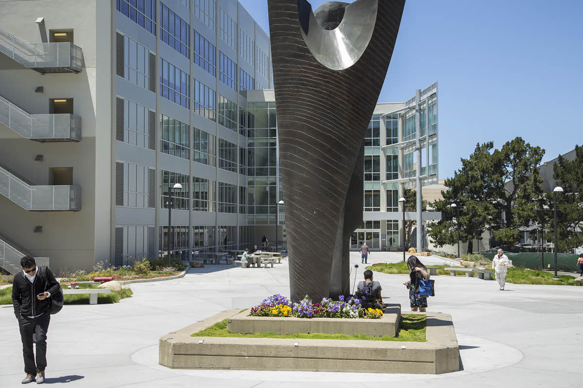 students walking by statue in front of library